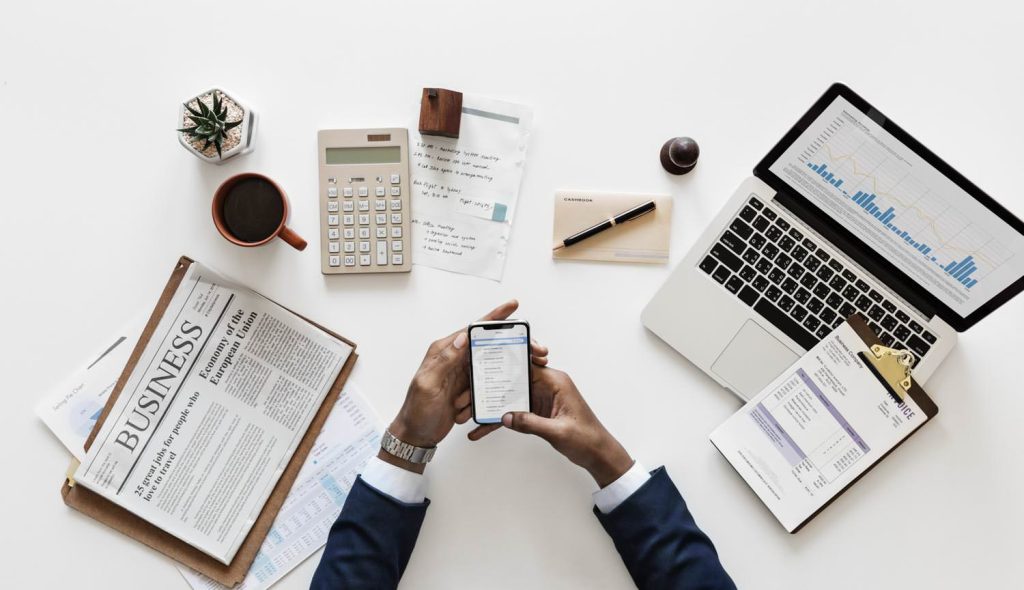 Man Holding Android Smartphone Near Macbook and Newspaper