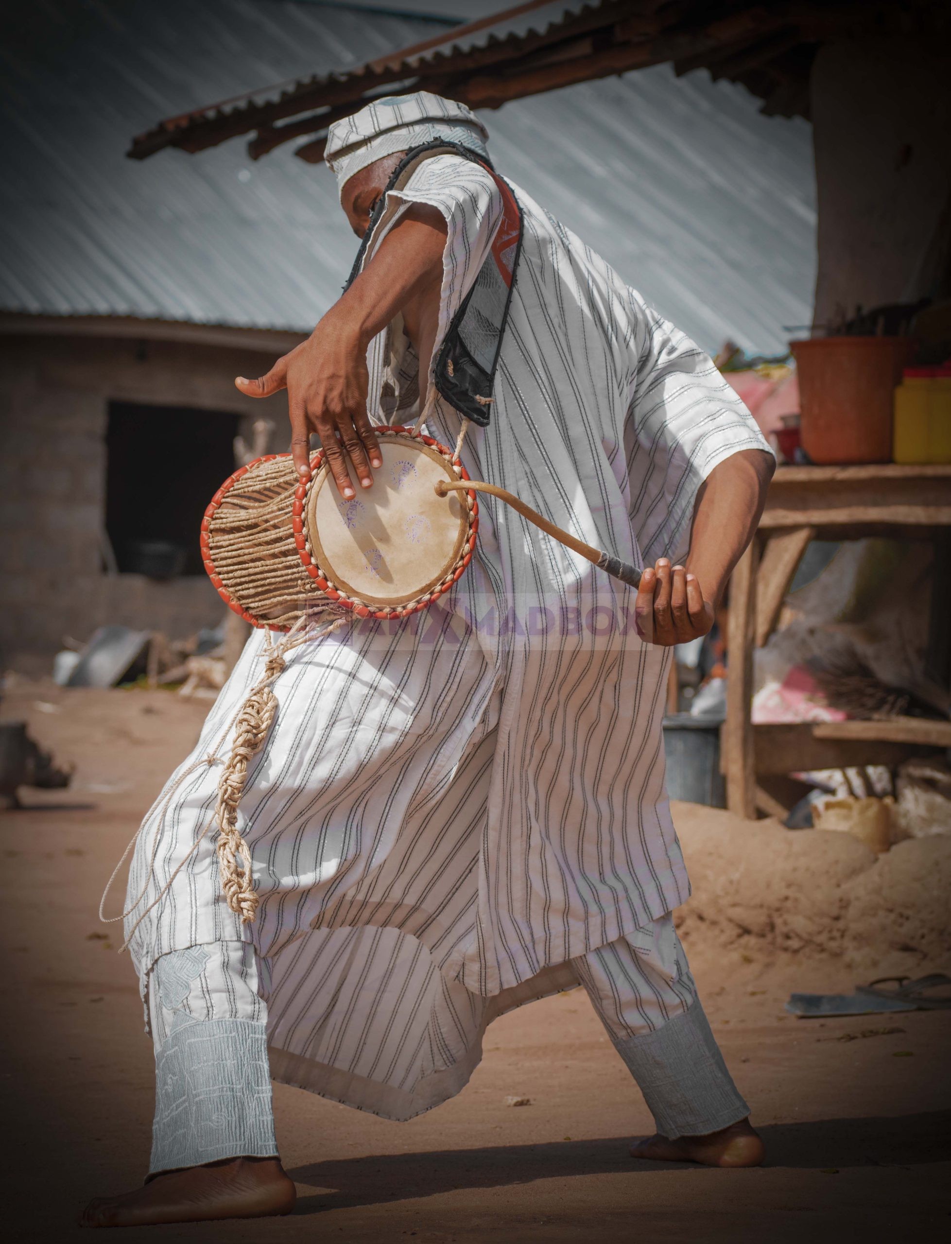 Ayangelu playing the talking drum in a village