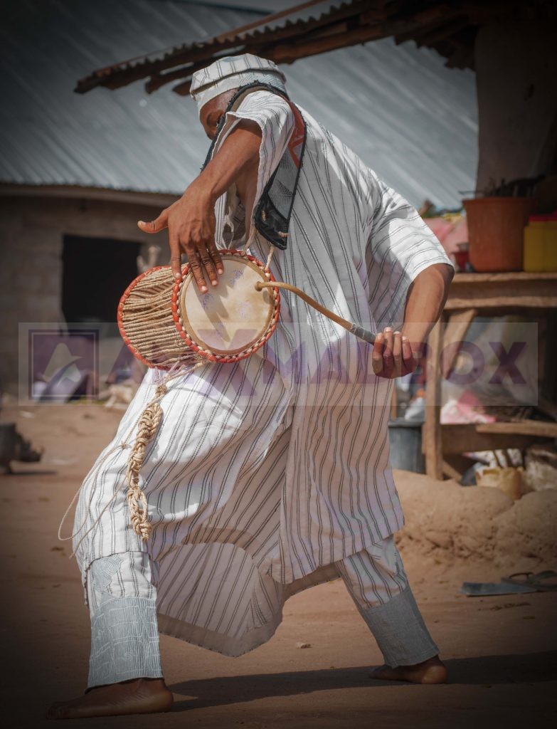 Ayangelu playing the talking drum in a village