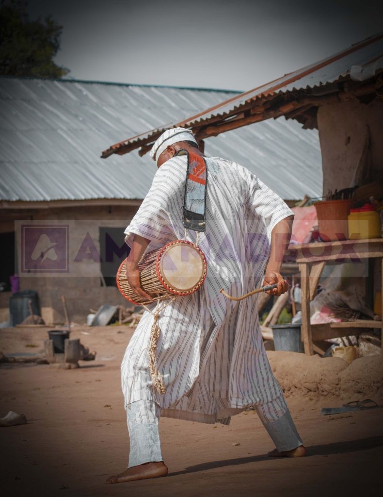 Yoruba Man playing the talking drum in a village